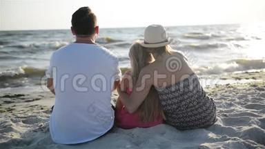 母亲、父亲和女儿坐在海边的海滩上，拥抱着太阳和波浪。